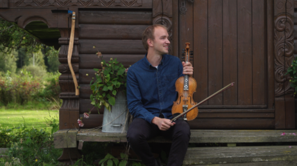 A white man earing a blue shirt and Black pants holds a fiddle