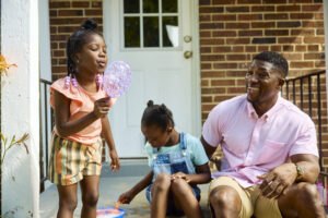 Adult and two children playing with bubbles outside.