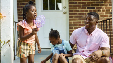 Adult and two children playing with bubbles outside.