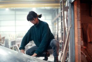 A young Asian woman, sat on her toes with her hair tied back, examining a piece of architecture in progress.