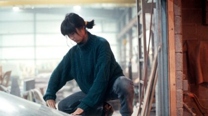 A young Asian woman, sat on her toes with her hair tied back, examining a piece of architecture in progress.
