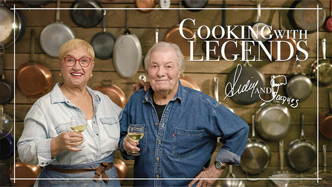 An older woman and an older man standing together with a drink in their hands.