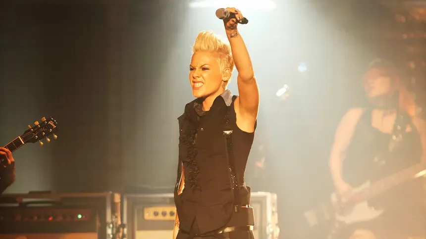 Singer Pink raising her mic to the audience as she performs on stage.