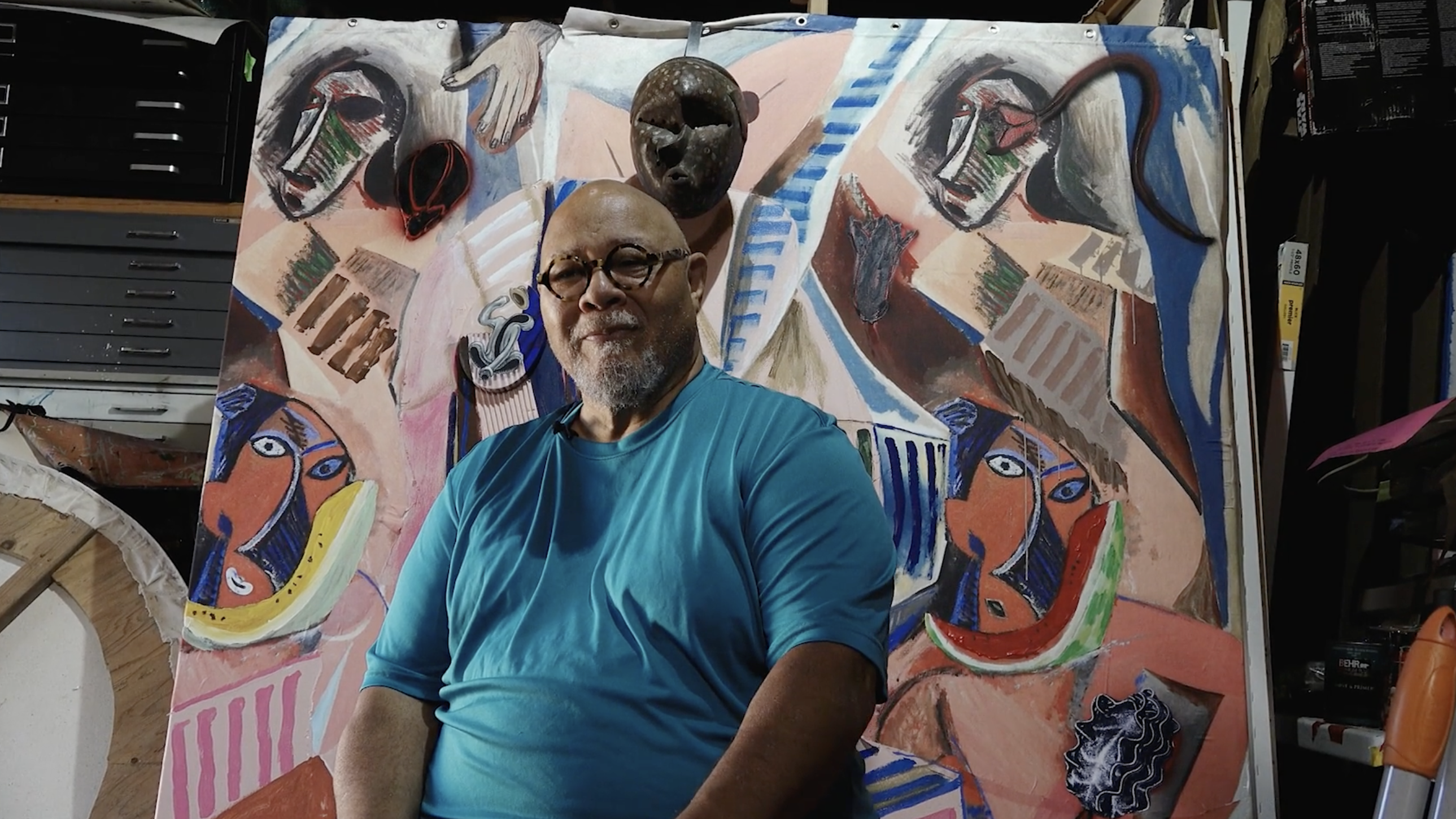 Artist Dewey Crumpler sitting in front of his painting.