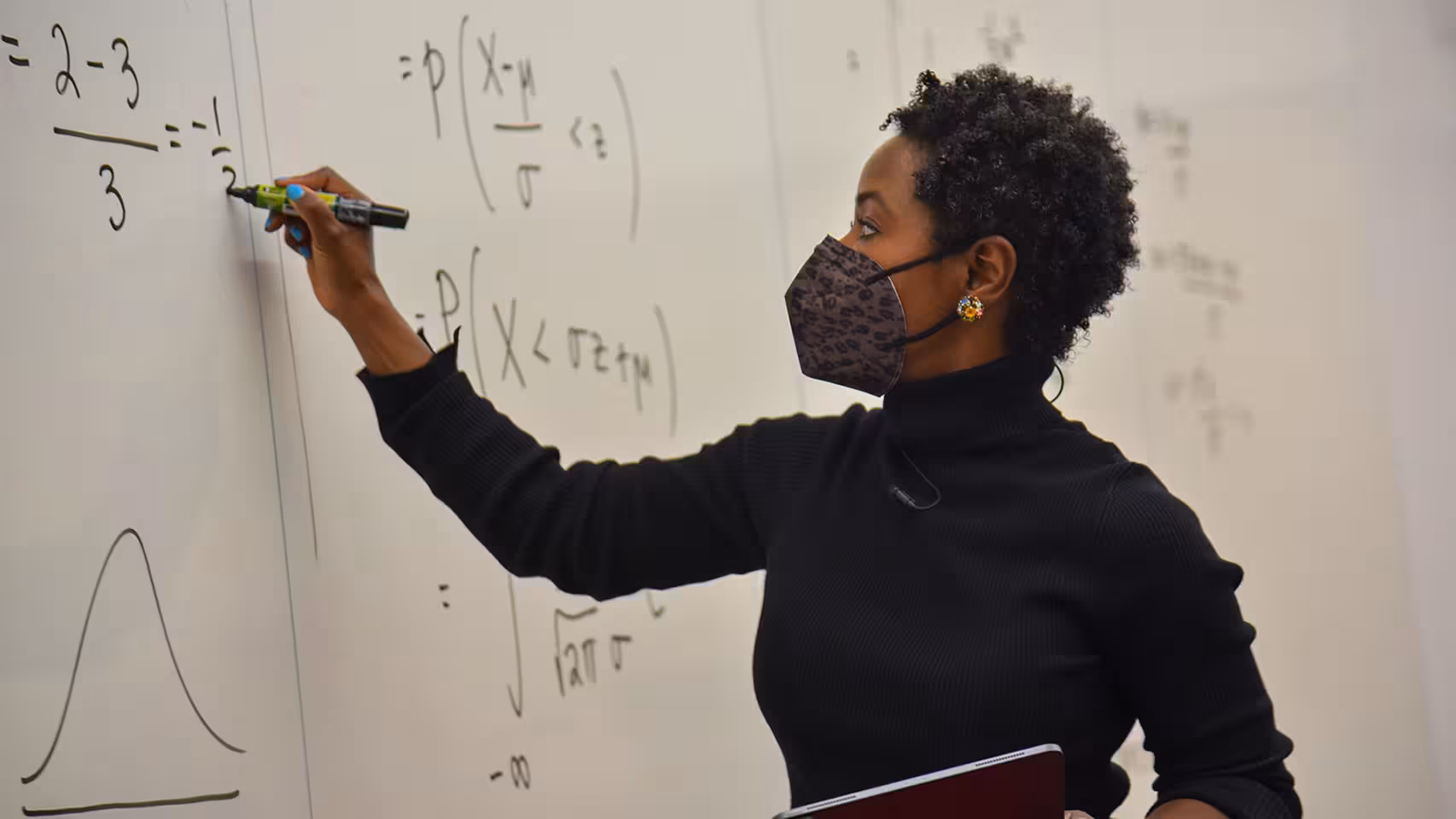 A Black woman with a mask on, writing on a white board