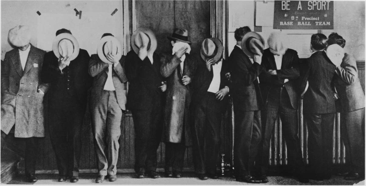 A group of men standing in a line hiding their faces with their hats.