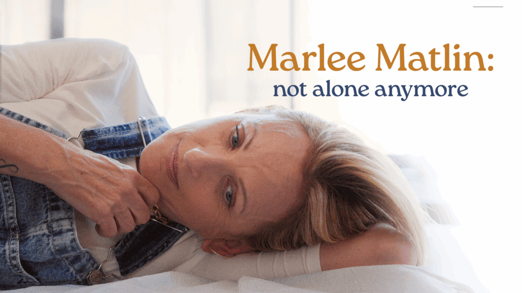 Actor Marlee Matlin wearing a shite t-shirt and overall jeans lying on a bed.