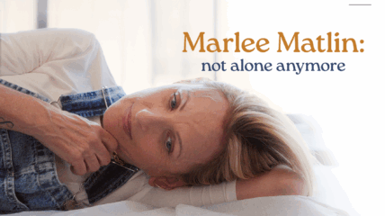 Actor Marlee Matlin wearing a shite t-shirt and overall jeans lying on a bed.