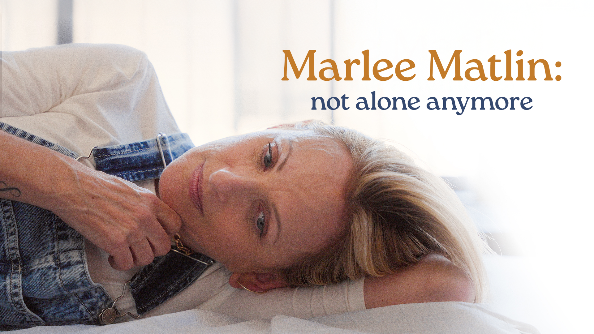 Actor Marlee Matlin wearing a shite t-shirt and overall jeans lying on a bed.