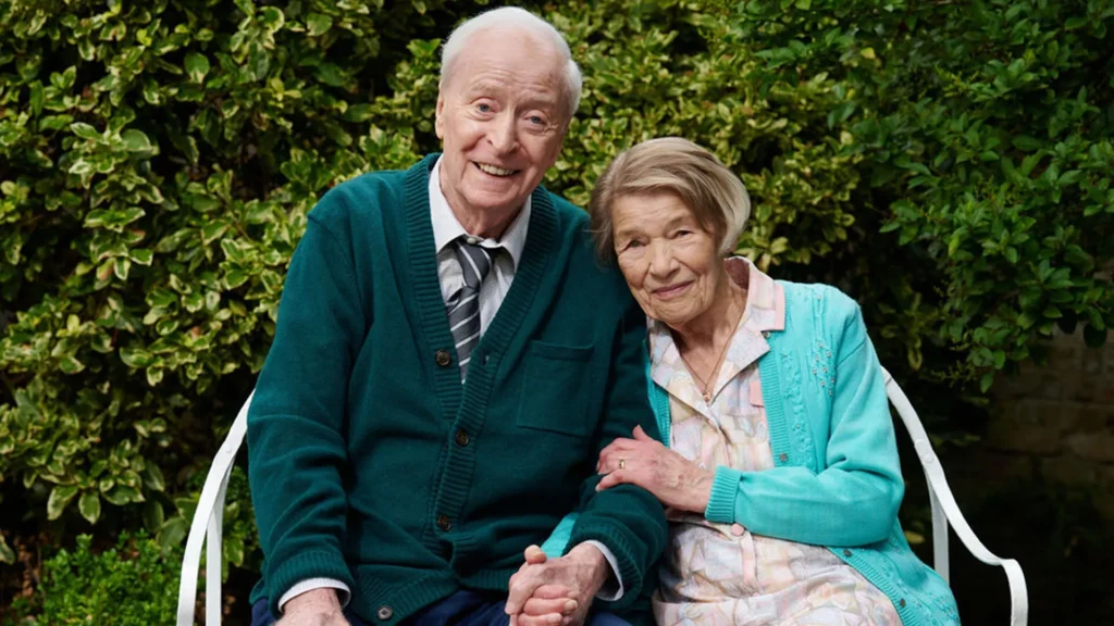 Actors Michael Caine and Glenda Jackson sitting together holding hands