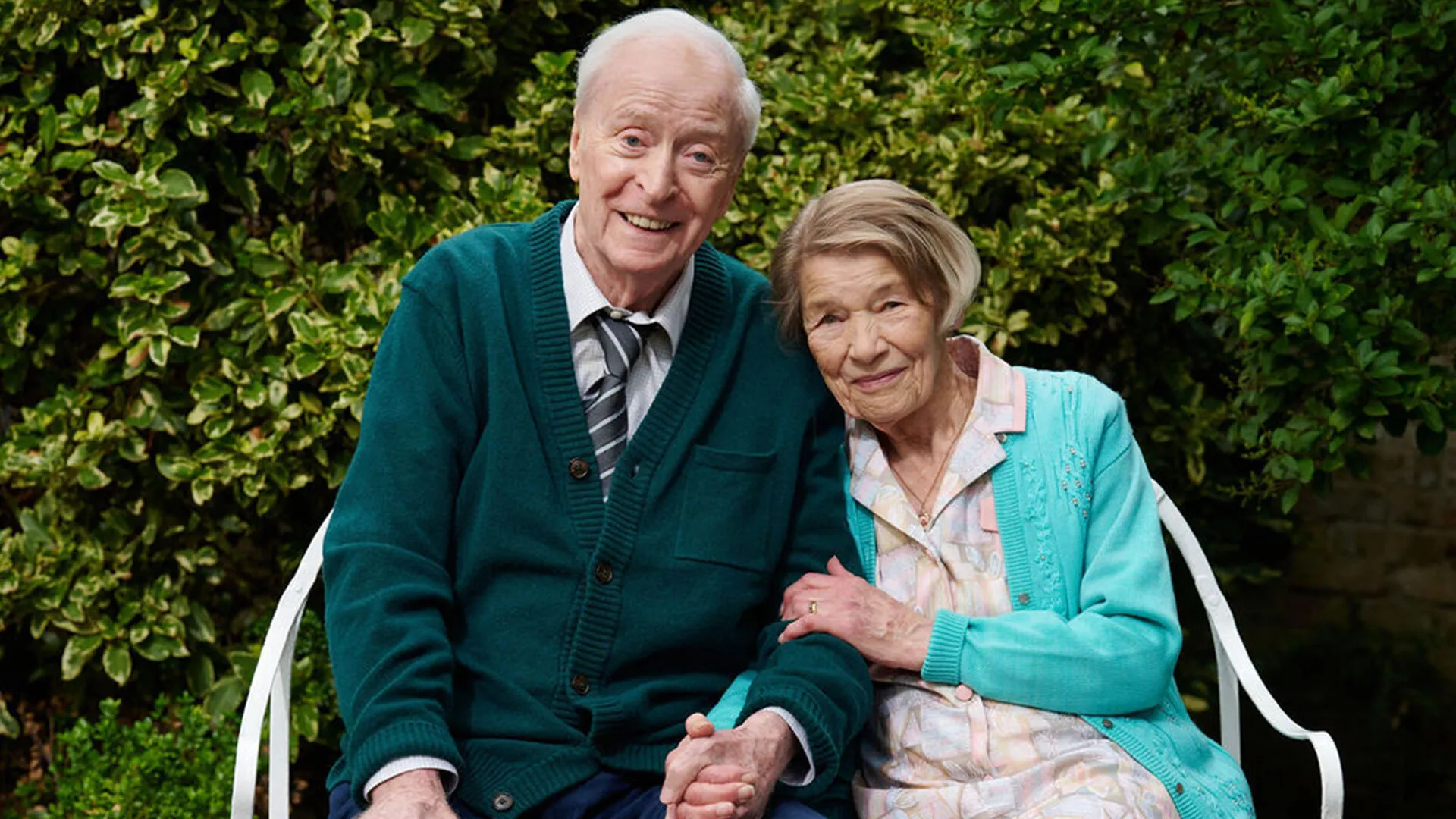 Actors Michael Caine and Glenda Jackson sitting together holding hands