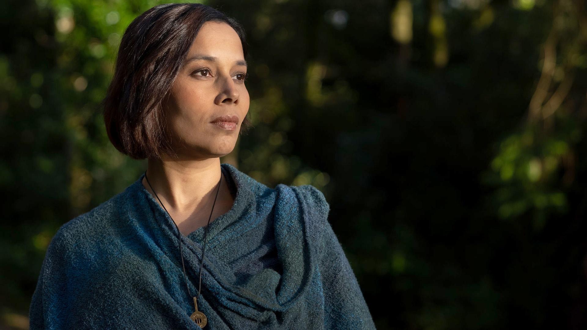 Rhiannon Giddens wearing a blue jacket with greenery behind her