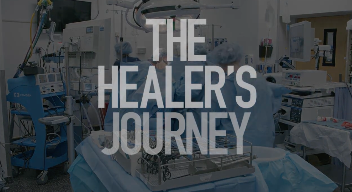 White type reads The Healer's Journey over a opaque photo of a surgery room with doctors working on a patient.