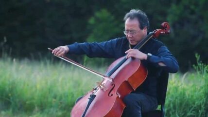 Yo-Yo Ma playing the cello in a grassy field