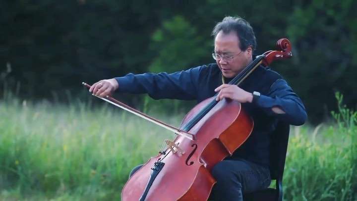 Yo-Yo Ma playing the cello in a grassy field