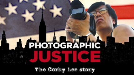 Corky Lee in a black ank and wearing black rimmed glasses holds a camera. Behind him is the American flag and in front of him is the silhouette of a city. Words over the city read Photographic Justice The Corky Lee Story