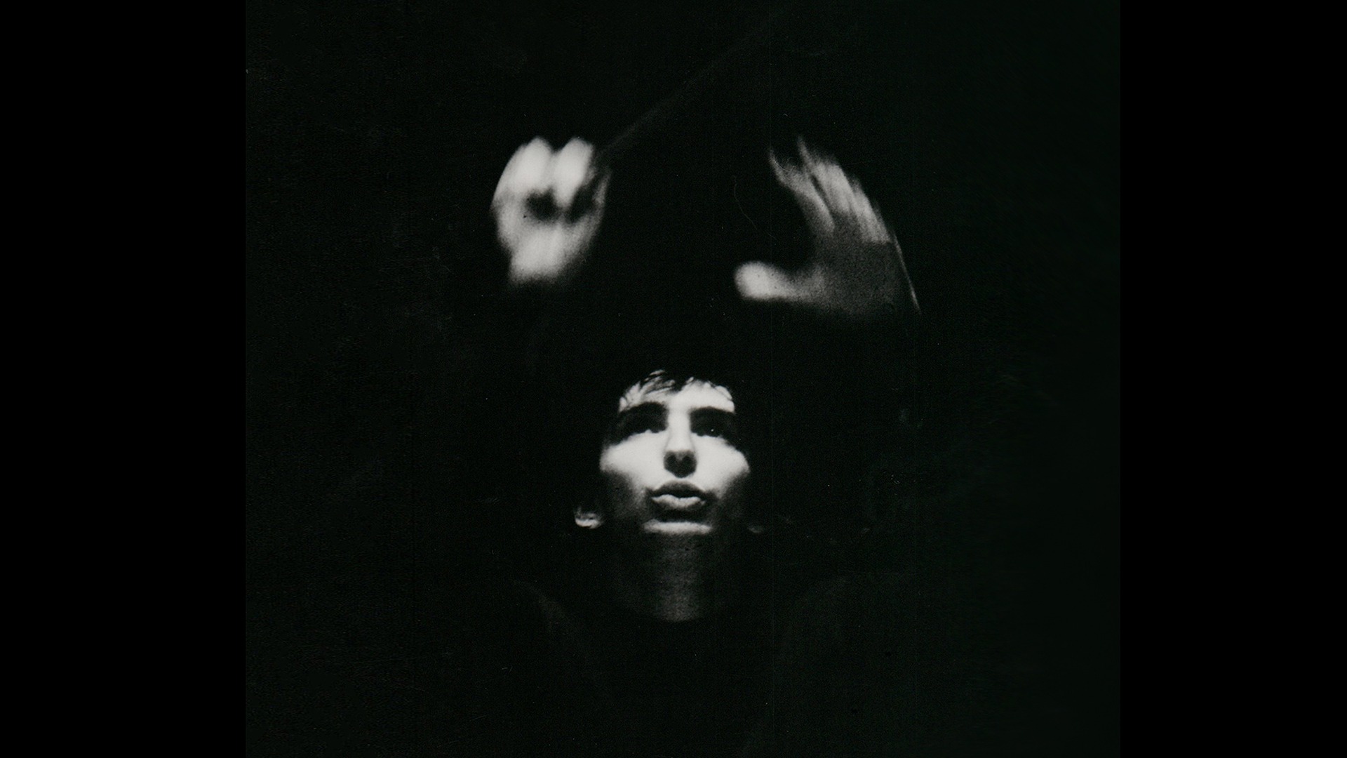 A black and white photo of Michael Tilson Thomas who is wearing all black with his hands both up in the air with a conductor's baton