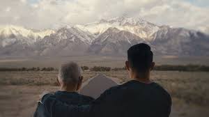 a son and his elderly father sitting side by sid looking out at snow capped mountias