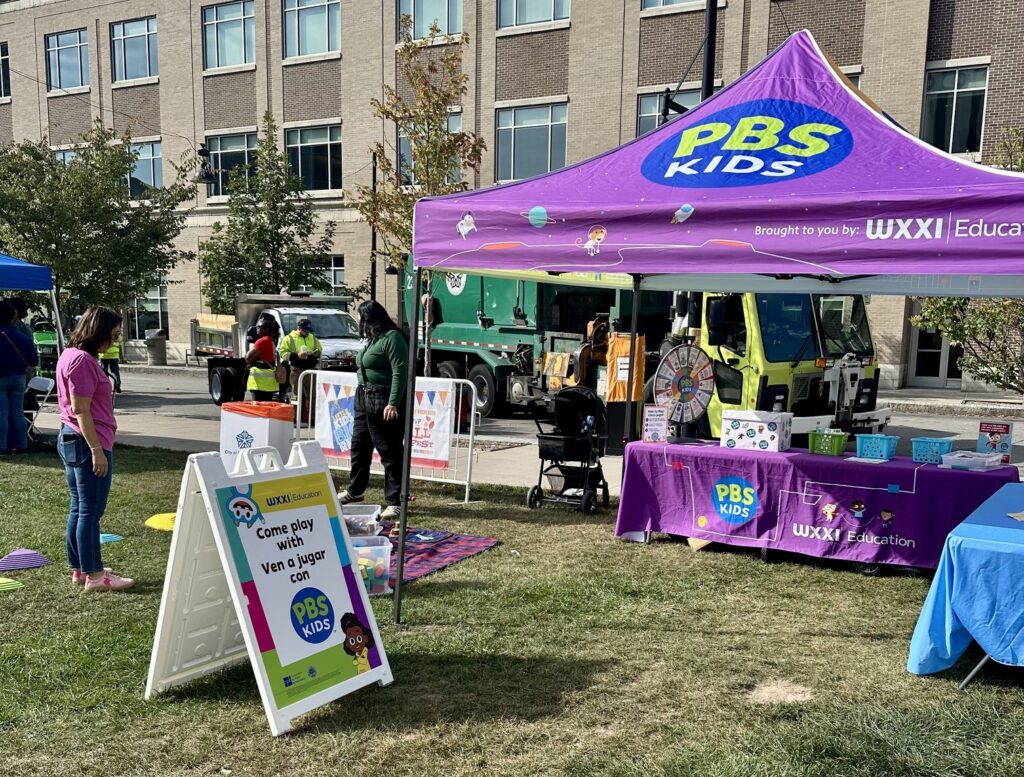 Purple PBS KIDS tent and sign at community event.