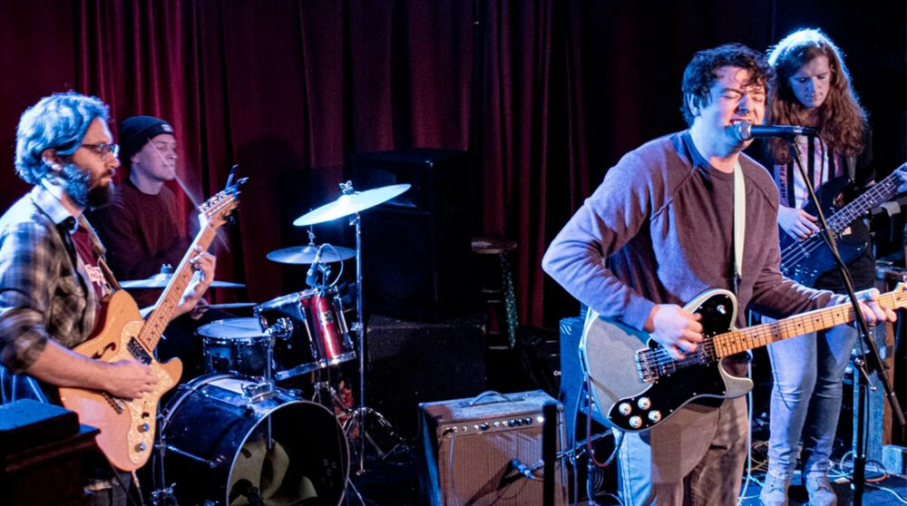 Four guys playing guitars and drums on a stage