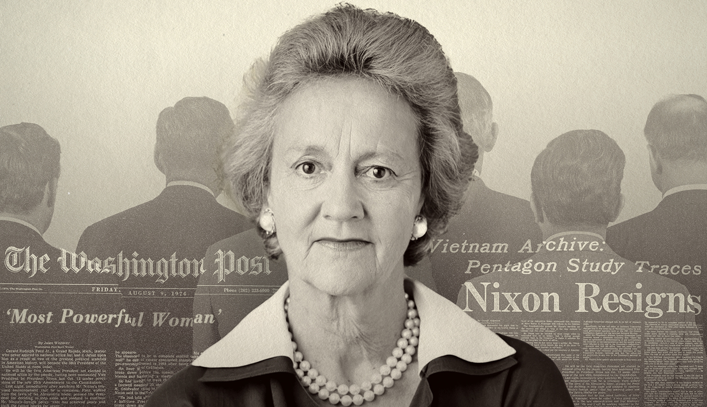 An older white woman with short gray hair wearing a string of pearls and a black dress with a white collar. Behind her is a screened back shot of the Washington Post.