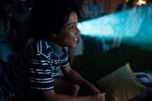Boy with striped shirt looking at movie projector.
