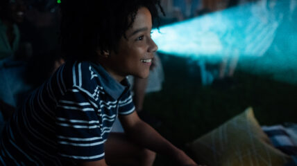 Boy with striped shirt looking at movie projector.