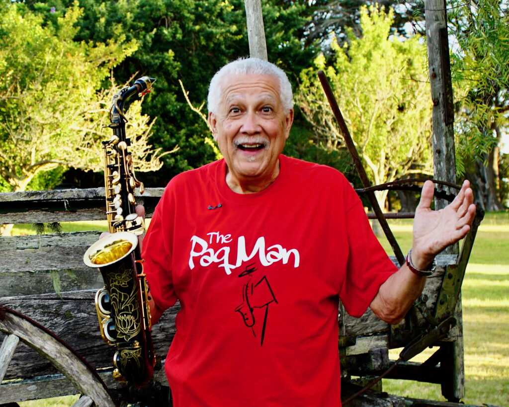 Paquito D'Riverain a red t-shirt holding his sax standing outside.