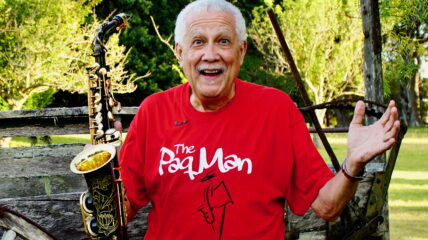 Paquito D'Riverain a red t-shirt holding his sax standing outside.