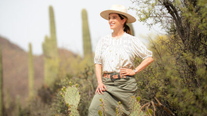 Pati Jinich standing in the filed of cacti wearng a white shirt , hat and green skirt