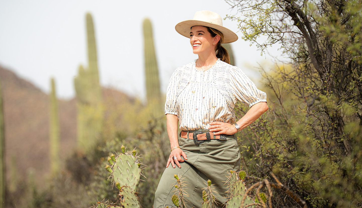 Pati Jinich standing in the filed of cacti wearng a white shirt , hat and green skirt